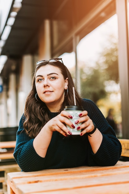 Retrato de uma jovem adulta com uma xícara de café perto de um café com bom tempo de outono