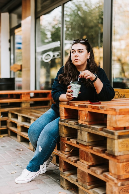 Retrato de uma jovem adulta com uma xícara de café perto de um café com bom tempo de outono