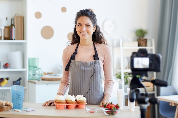 Retrato de uma jovem adulta de pé à mesa da cozinha com cupcakes caseiros com creme de manteiga.