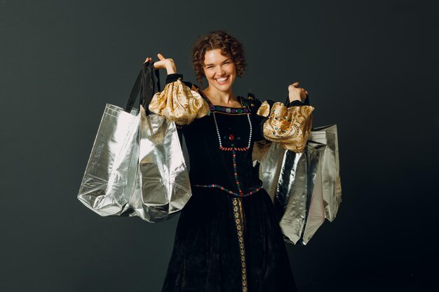 Retrato de uma jovem adulta sorridente vestida com um vestido medieval segurando sacos de compras nas mãos