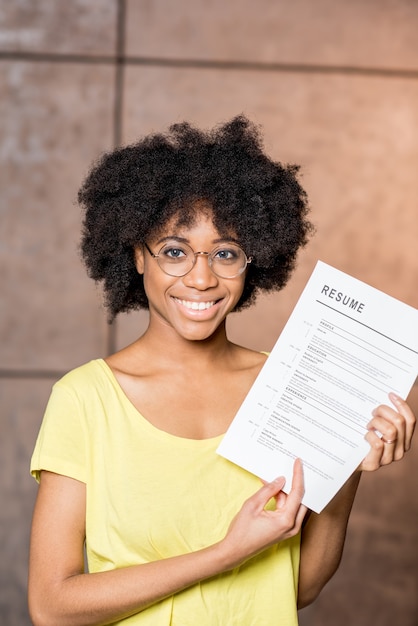 Foto retrato de uma jovem africana segurando o documento de currículo dentro de casa