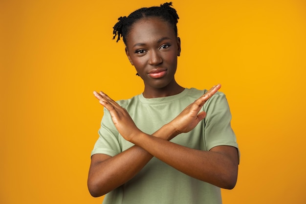 Retrato de uma jovem africana séria mostrando gesto de parada no estúdio amarelo