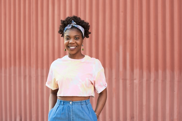 Retrato de uma jovem africana sorrindo para a câmera em pé ao ar livre contra a parede