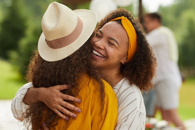 Foto retrato de uma jovem afro-americana abraçando um amigo e sorrindo alegremente enquanto desfruta de uma festa ao ar livre no verão