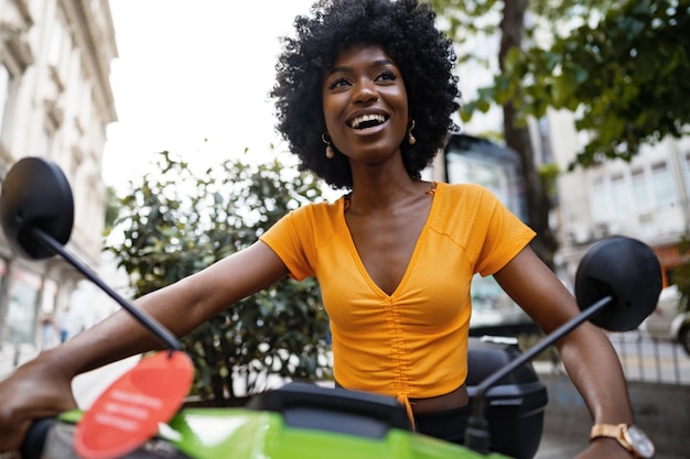 Retrato de uma jovem afro-americana andando de moto verde na cidade