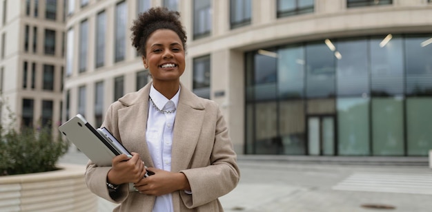 Retrato de uma jovem afro-americana bem-sucedida com um laptop nas mãos e um sorriso largo
