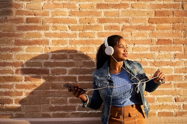 Retrato de uma jovem afro-americana com fones de ouvido, ouvindo música em seu telefone celular