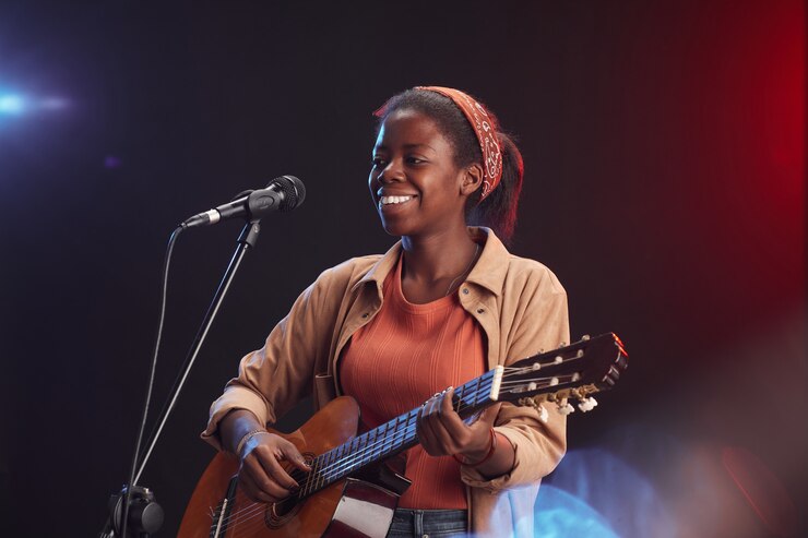 Foto retrato de uma jovem afro-americana tocando guitarra no palco e cantando para o microfone, sorrindo, copie o espaço