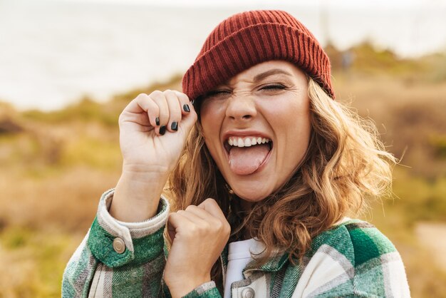 Retrato de uma jovem alegre, caucasiana, usando chapéu e camisa xadrez, sorrindo enquanto caminha ao ar livre