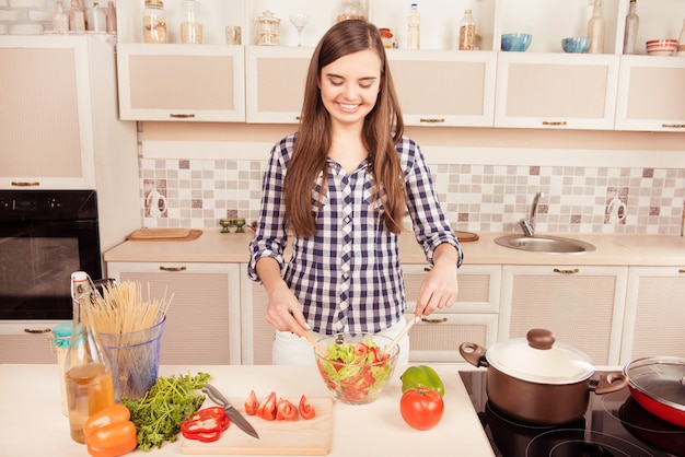 Retrato de uma jovem alegre cozinhando e misturando salada