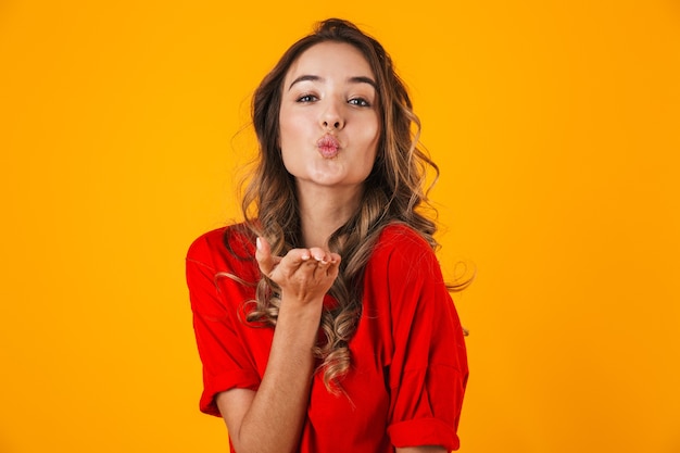 Foto retrato de uma jovem alegre e adorável em pé isolado na parede amarela, mandando um beijo
