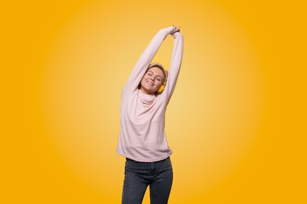 Retrato de uma jovem alegre e estilosa isolada sobre fundo amarelo ouvindo música com fones de ouvido dançando