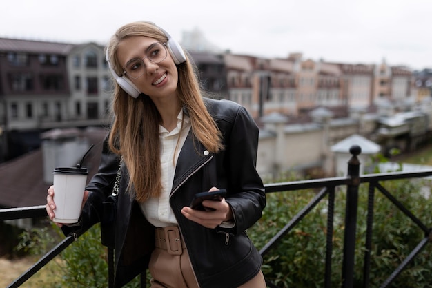 Retrato de uma jovem alegre e feliz com um telefone celular e uma xícara de café nas mãos