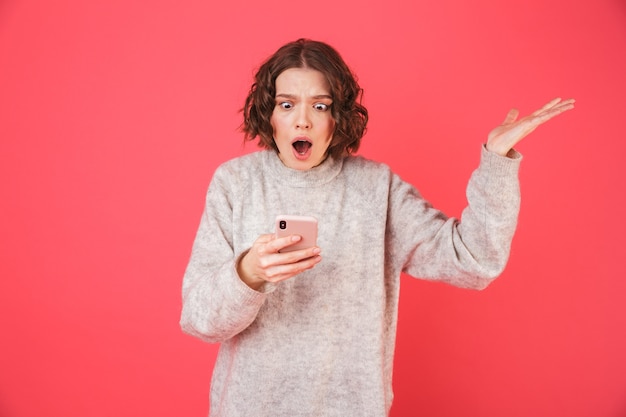 Retrato de uma jovem alegre em pé isolado sobre a rosa, segurando um telefone celular