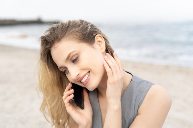 Retrato de uma jovem alegre falando em um telefone celular com um sorriso fofo na praia