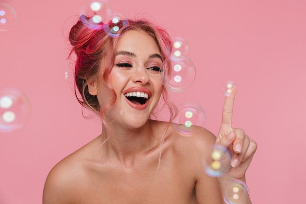 Retrato de uma jovem alegre sem camisa, sorrindo e posando com bolhas de sabão