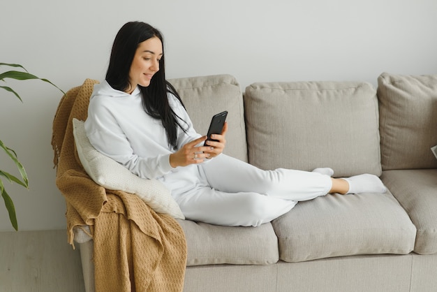 Retrato de uma jovem alegre usando o celular enquanto relaxa no sofá em casa