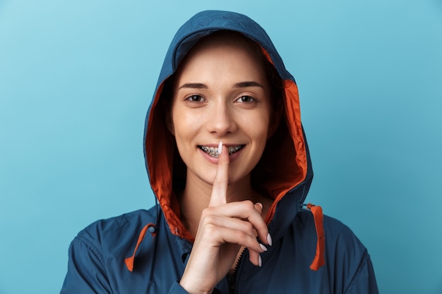 Retrato de uma jovem alegre, vestindo uma capa de chuva, isolado na parede azul