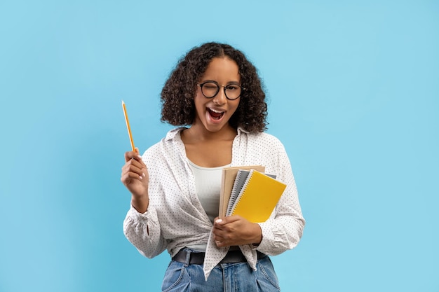 Foto retrato de uma jovem aluna alegre com notebooks tendo uma ótima ideia apontando o lápis para cima e