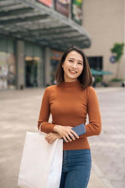 Retrato de uma jovem asiática alegre com sacolas de compras no shopping ao ar livre