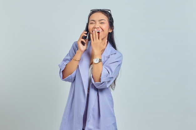 Retrato de uma jovem asiática alegre falando no celular com as mãos cobrindo a boca isolada no fundo branco