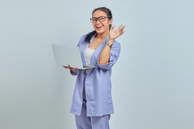 Retrato de uma jovem asiática alegre usando laptop e gesticulando mão de onda isolada em fundo branco