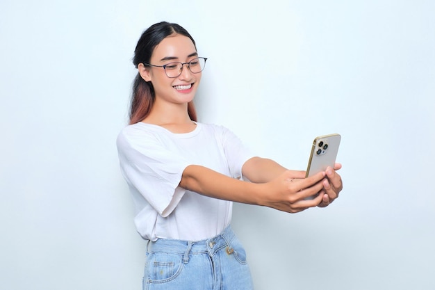 Retrato de uma jovem asiática animada em camiseta branca usando telefone celular isolado em fundo branco