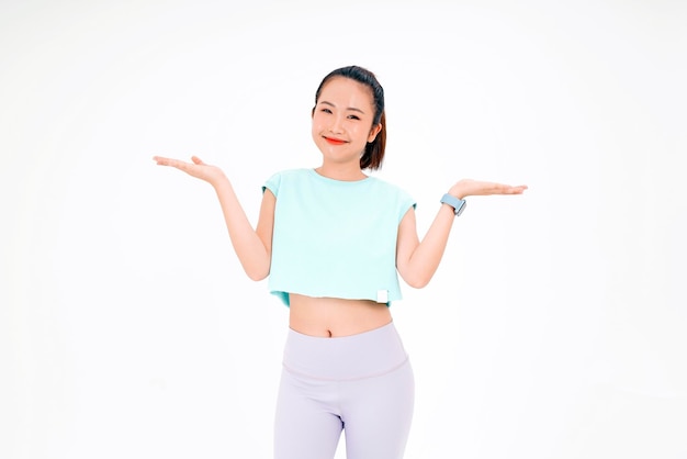 Retrato de uma jovem asiática bonita e alegre em roupas de ginástica com ponto de dedo no espaço de cópia isolado no fundo