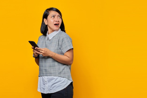 Retrato de uma jovem asiática chocada e surpresa segurando um telefone celular e olhando de soslaio