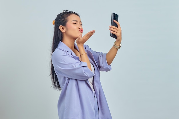 Retrato de uma jovem asiática encantadora de mãos dadas mandando beijo aéreo para namorado enquanto fazia videochamada em fundo branco