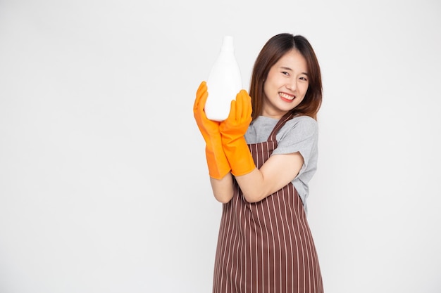 Retrato de uma jovem asiática feliz empregada doméstica ou dona de casa usando luvas de borracha e segurando produtos de limpeza isolados no fundo branco