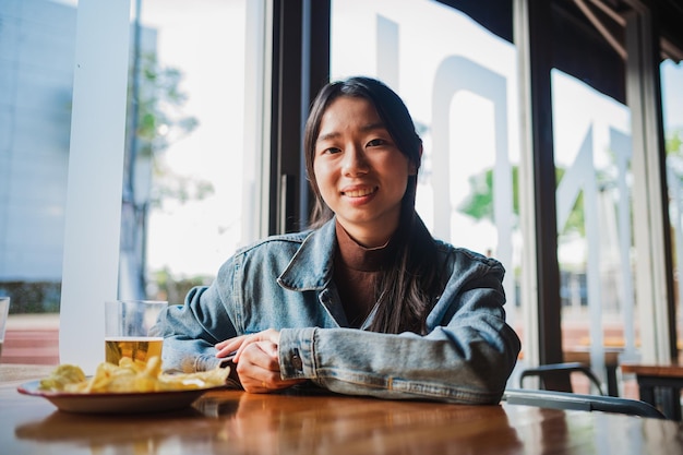 Retrato de uma jovem asiática feliz olhando para a câmera Ela está em um bar tomando uma cerveja
