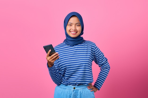 Retrato de uma jovem asiática feliz segurando um smartphone no fundo rosa