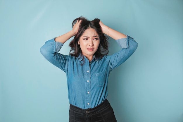 Retrato de uma jovem asiática isolada por fundo azul, sentindo-se frustrada com a expressão do rosto indefeso