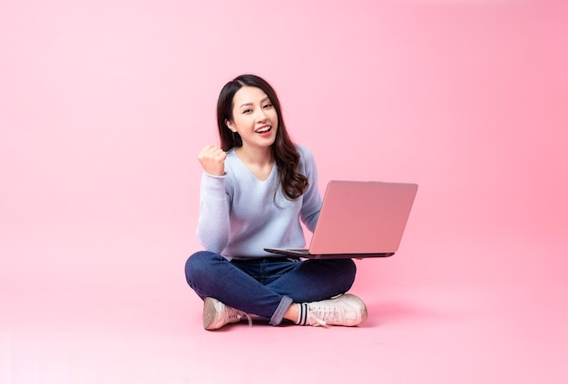 Retrato de uma jovem asiática sentada usando um laptop, isolado em um fundo rosa