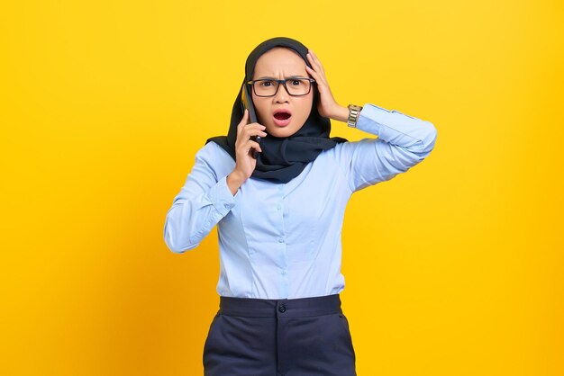 Retrato de uma jovem asiática surpresa falando no celular com a boca aberta, uma notícia incrível de reação isolada em fundo amarelo