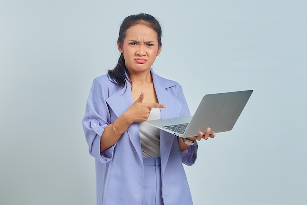 Retrato de uma jovem asiática triste apontando dedos para um laptop e olhando para a câmera isolada em fundo branco