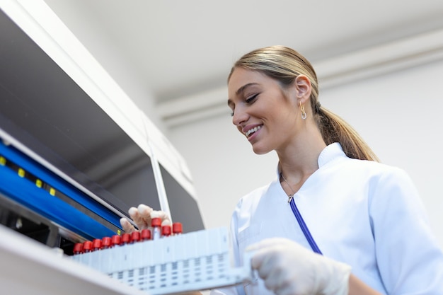 Retrato de uma jovem assistente de laboratório fazendo análises com tubos de ensaio e analisadores sentados no laboratório moderno