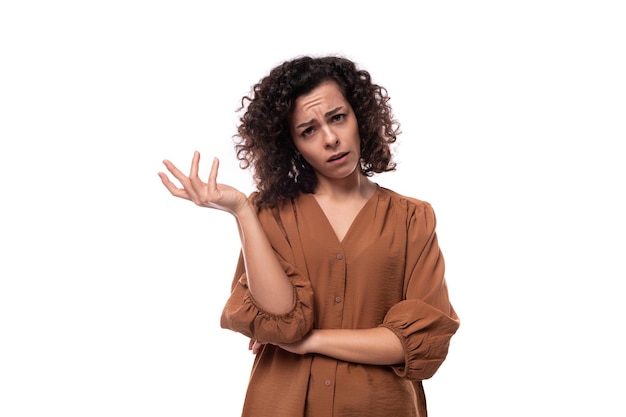 Foto retrato de uma jovem assistente morena encaracolada vestida com uma camisa marrom em um fundo branco