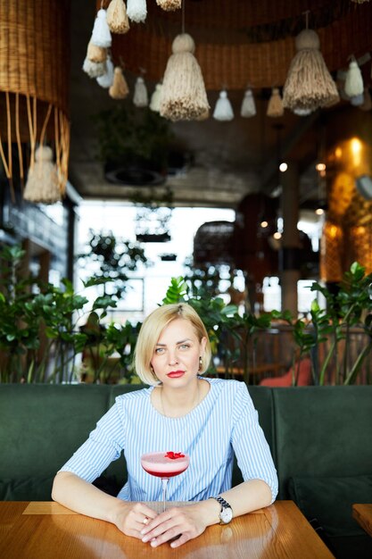 Retrato de uma jovem atraente bebendo coquetel no café interior Linda loira relaxando no bar e bebendo um coquetel