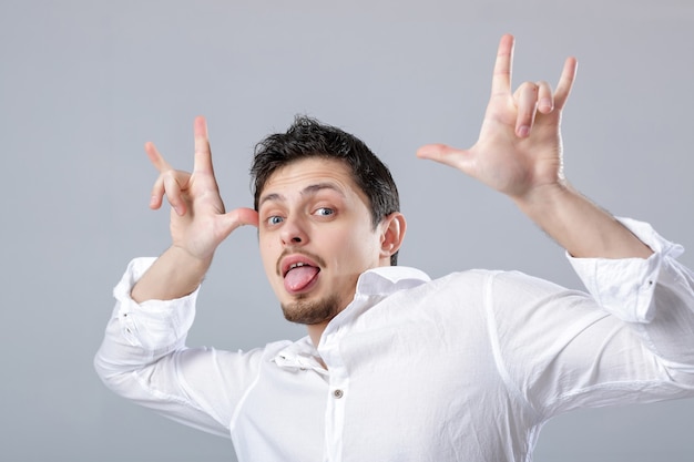 Retrato de uma jovem atraente com cabelos escuros na camisa branca, brincando sobre o fundo cinza.