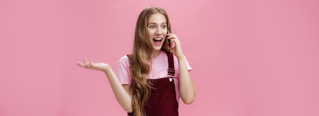 Foto retrato de uma jovem atraente, extrovertida e falante, popular, de macacão, acenando com a mão levantada durante