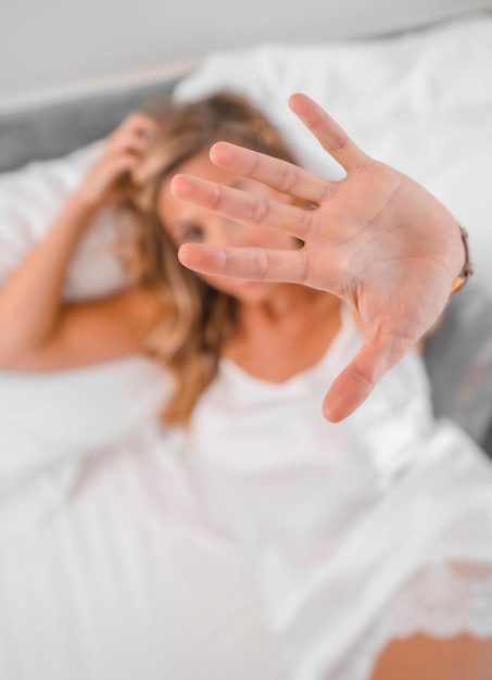 Retrato de uma jovem atraente loira caucasiana de camisola na cama, colocando a mão para a câmera