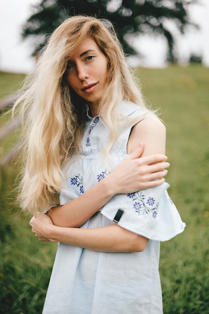 Foto retrato de uma jovem atraente loira elegante em um vestido azul romântico posando sobre o fundo do campo