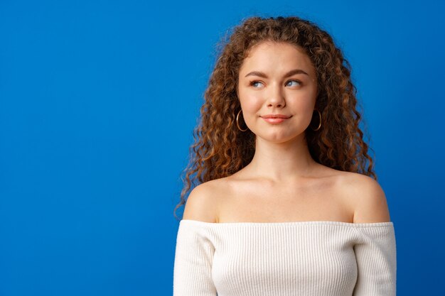 Retrato de uma jovem atraente mulher de cabelos cacheados contra um fundo azul.