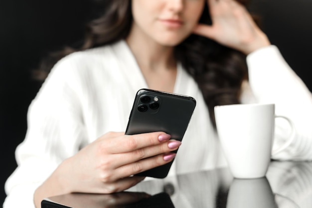 Retrato de uma jovem atraente navegando nas mídias sociais ou notícias em um café Uma jovem olha para o telefone e segura uma caneca de café Fechar