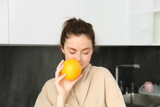 Retrato de uma jovem atraente posando com uma laranja bebendo suco fresco em casa na cozinha