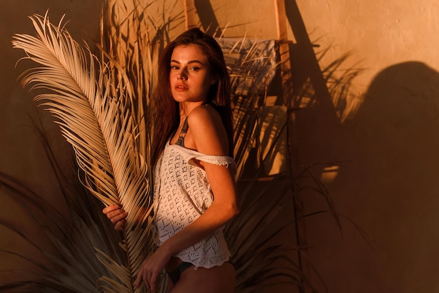 Retrato de uma jovem atraente posando e desfrutando de uma folha de palmeira coberta do lado de fora de uma casa tropical
