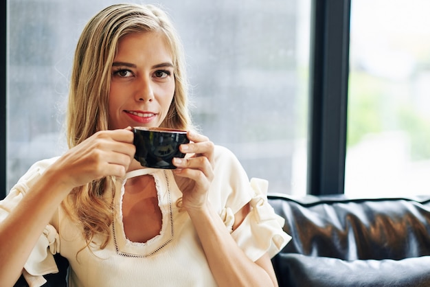 Foto retrato de uma jovem atraente sorridente, desfrutando de uma xícara de café preto quente