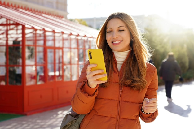 Retrato de uma jovem atraente sorridente usando smartphone na rua no inverno